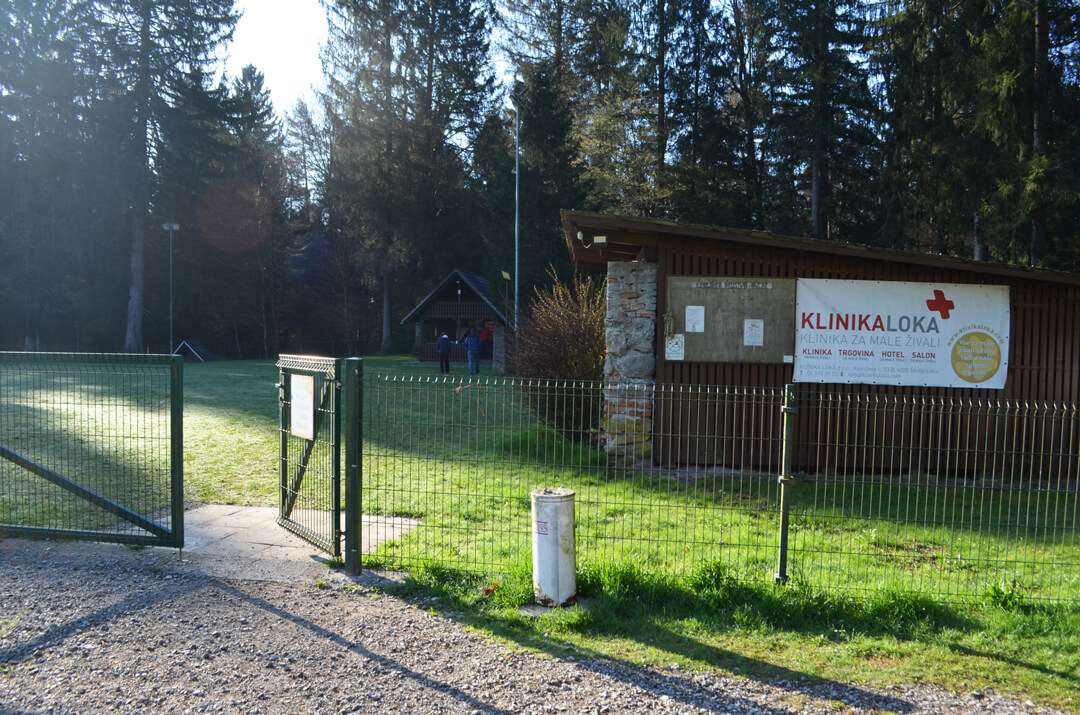 Vhod na poligon z ograjo in tablo z napisom.